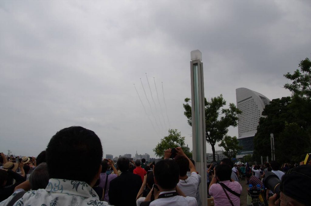 パシフィコ横浜前の臨港パークで待つ大勢の観客に向かって、スモークを引き、フォーメーションを組んで飛来するブルーインパルス
